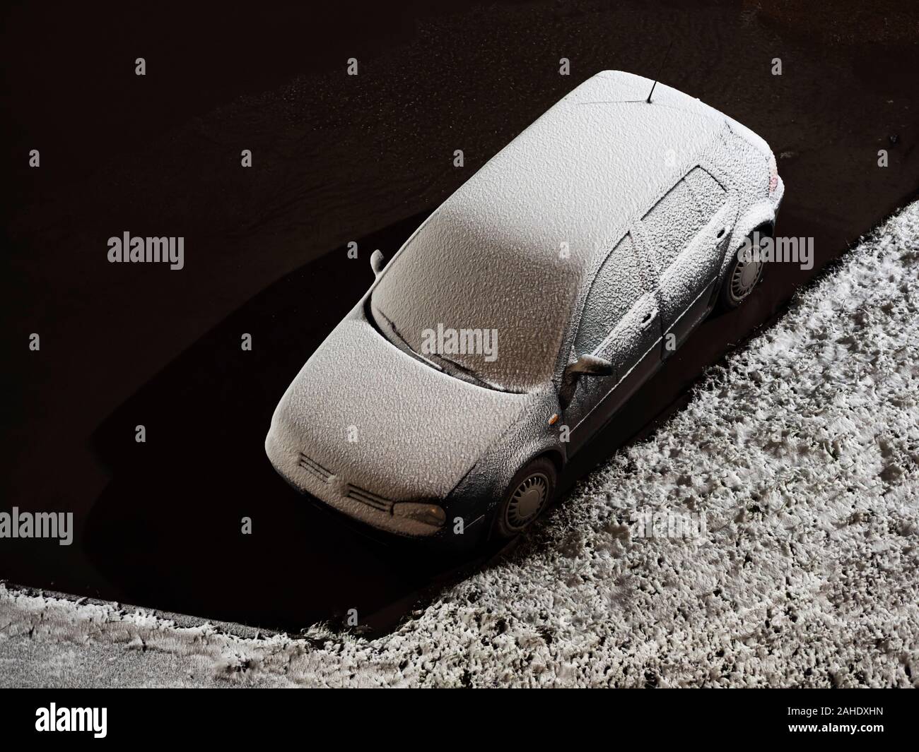 Une voiture couverte de neige fraîchement tombée se trouve dans une flaque d'eau près d'une pelouse couverte de neige Banque D'Images