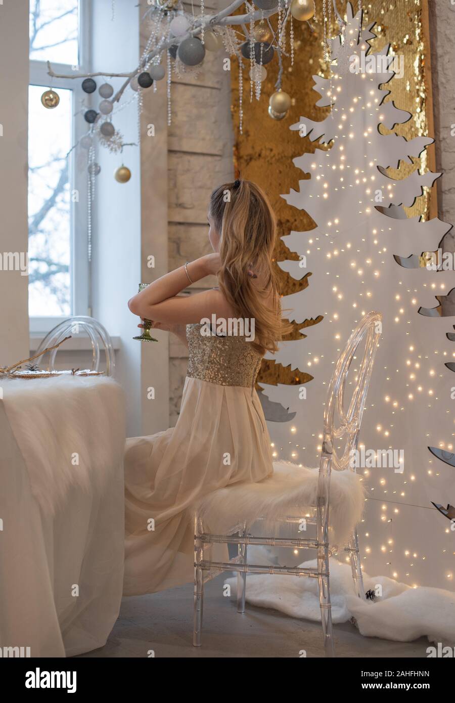 Jeune fille dans une robe de soirée. La fille est de rêver. La veille de Noël. Maison de vacances confortable au sapin avec des lumières et décoration dorée. fille dans une robe brillante sur Banque D'Images