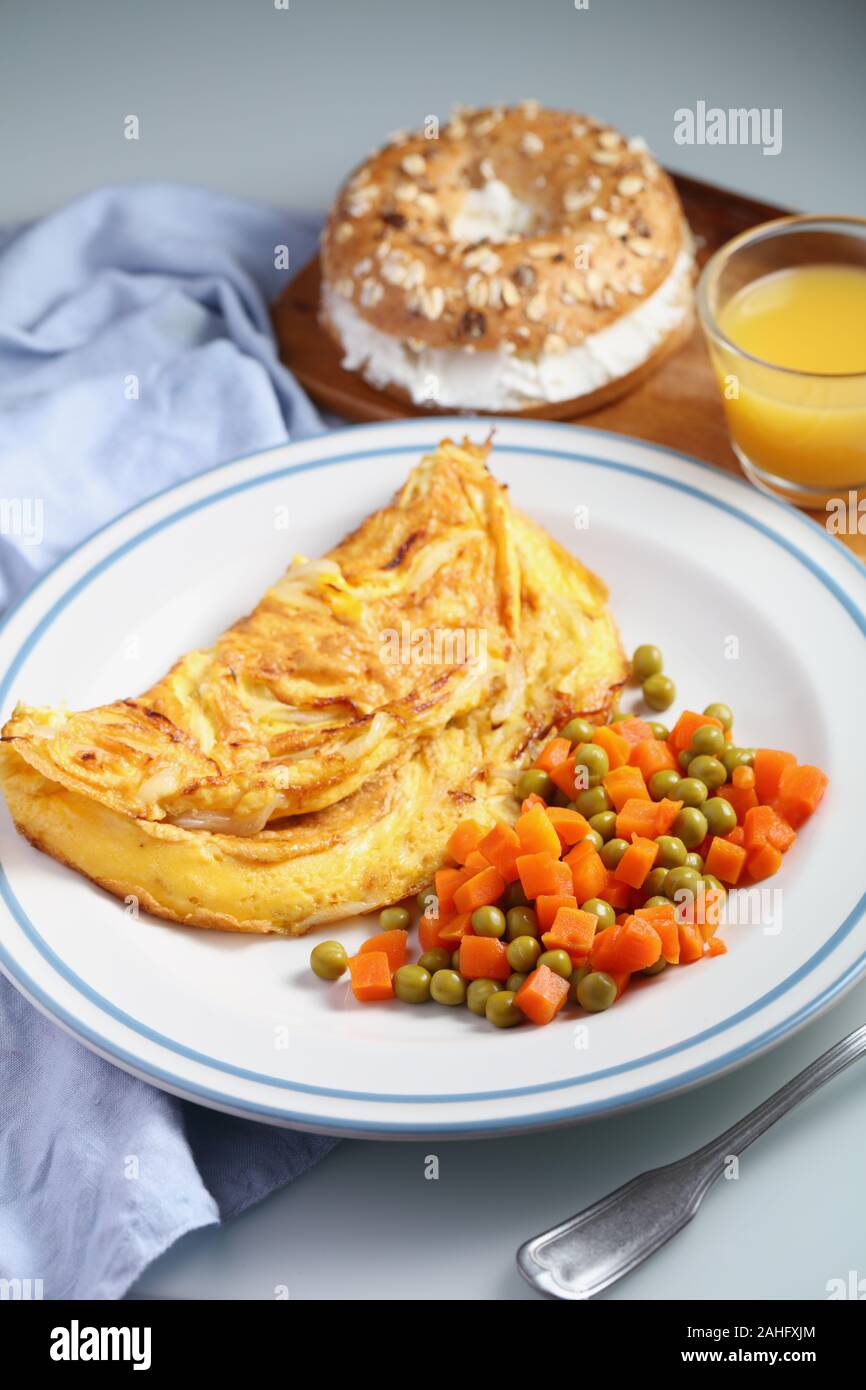 Petit déjeuner avec omelette française, salade de petits pois et carottes, sandwich au bagel au fromage doux et une tasse de jus d'orange en gros plan Banque D'Images