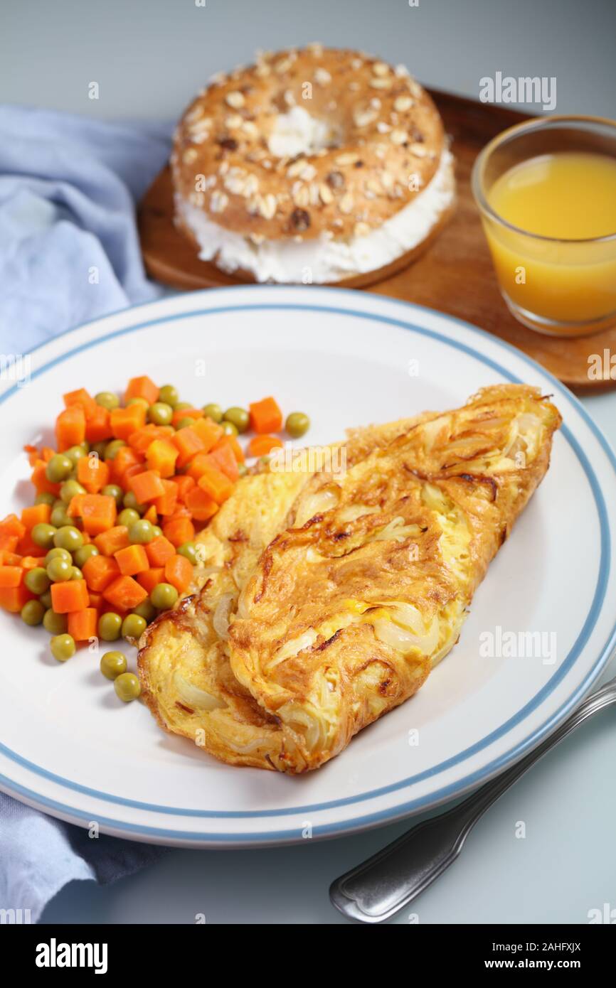 Petit déjeuner avec omelette française, salade de petits pois et carottes, sandwich au bagel au fromage doux et une tasse de jus d'orange en gros plan Banque D'Images