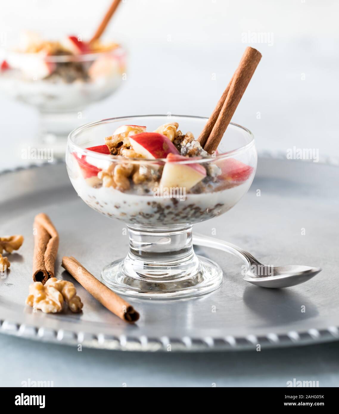 Une vue en gros plan d'un plat en verre de coupe Acier mélangé avec de l'avoine, les graines de chanvre et les graines de chia et surmontée de pommes en dés, les noix et les bâtons de cannelle. Banque D'Images