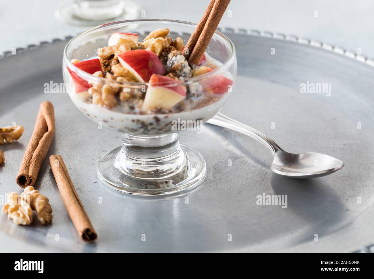 Un gros plan de coupe en acier plat de verre mélangé avec de l'avoine, les graines de chanvre et les graines de chia et garni avec des morceaux de pommes, les noix et la cannelle. Banque D'Images