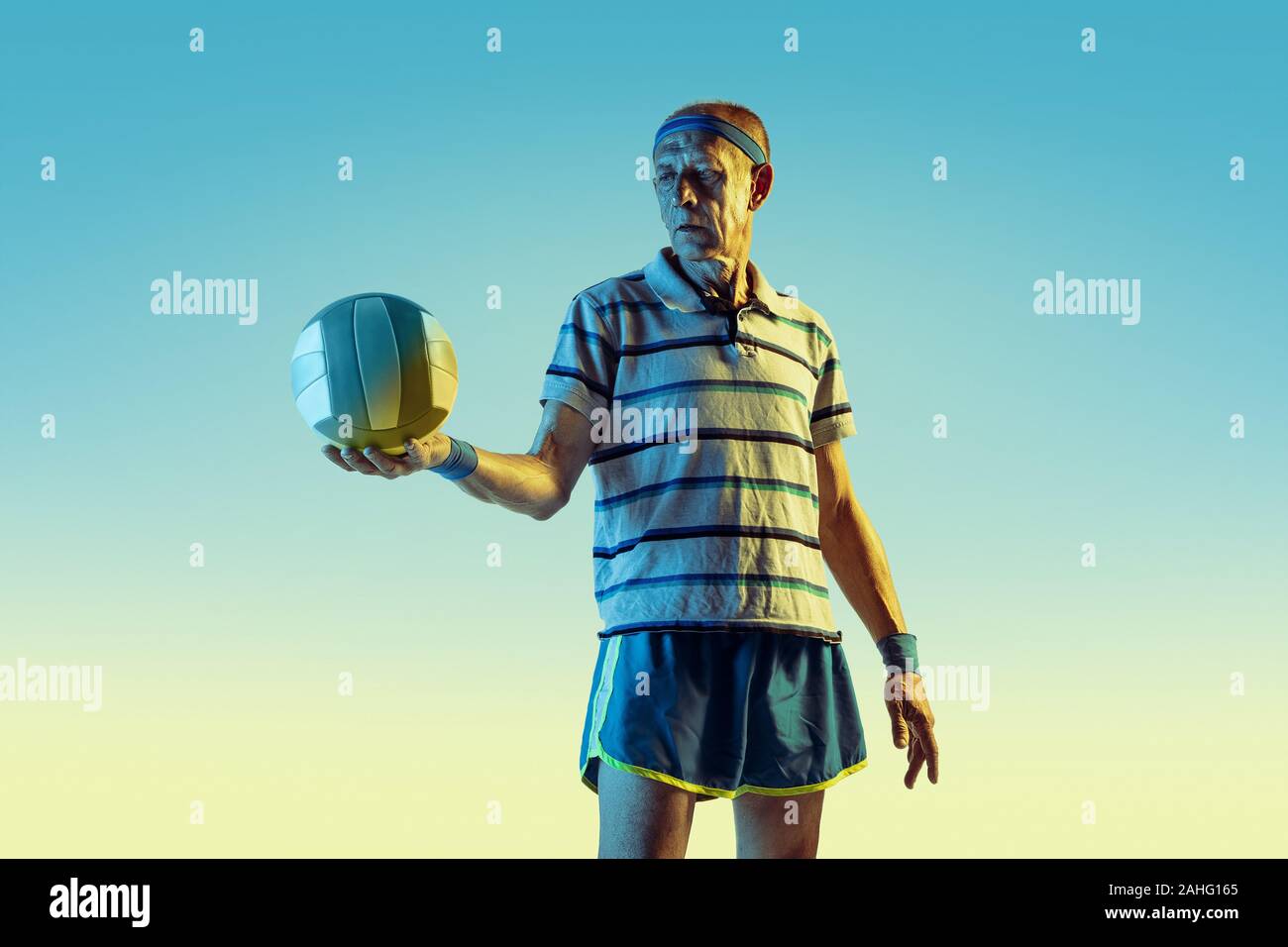 Senior man wearing sportwear jouer au volley-ball sur fond dégradé, neon light. Modèle homme de race blanche dans la grande forme reste actif. Concept de sport, activité, mouvement, bien-être, la confiance. Banque D'Images