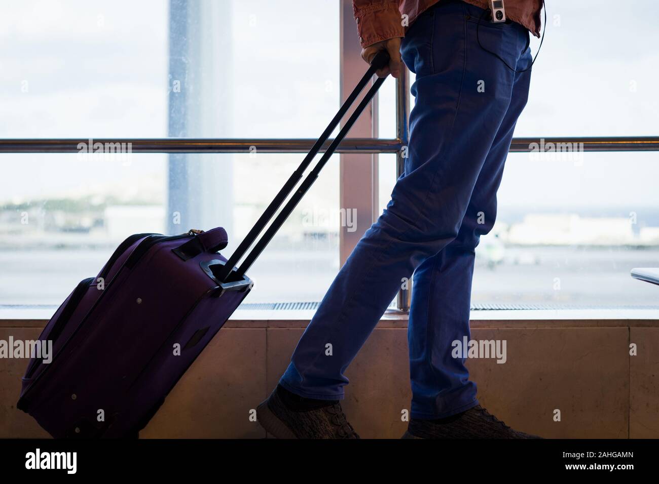 L'homme sur les jeans avec transporter sur valise à Las Palmas terminal de  l'aéroport. Zone d'atterrissage sur l'avion en tant que passager passe par  l'écoute de musique sur lecteur mp3 Photo Stock -
