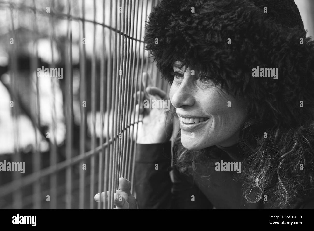 Charmante dame d'âge moyen avec chapeau en fourrure russe tenant à la clôture avec sourire observer la faune au zoo parc. Concept de vente de mode de chute. Noir et blanc Banque D'Images