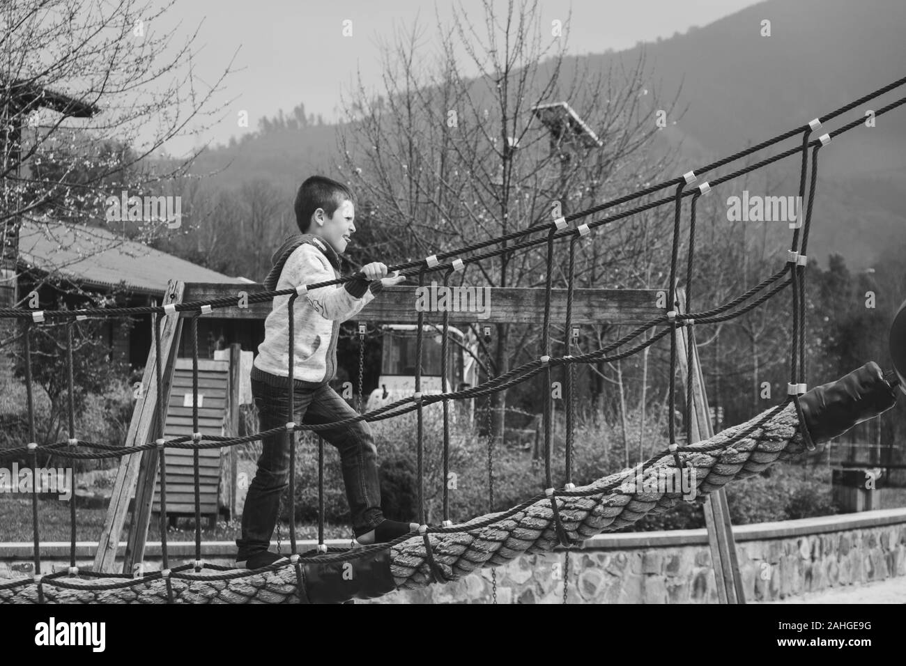 Jeune garçon traversant le pont tout en tenant aux cordes au parc de Bilbao. Photographie noir et blanc. Gamin à l'aire de jeux Banque D'Images