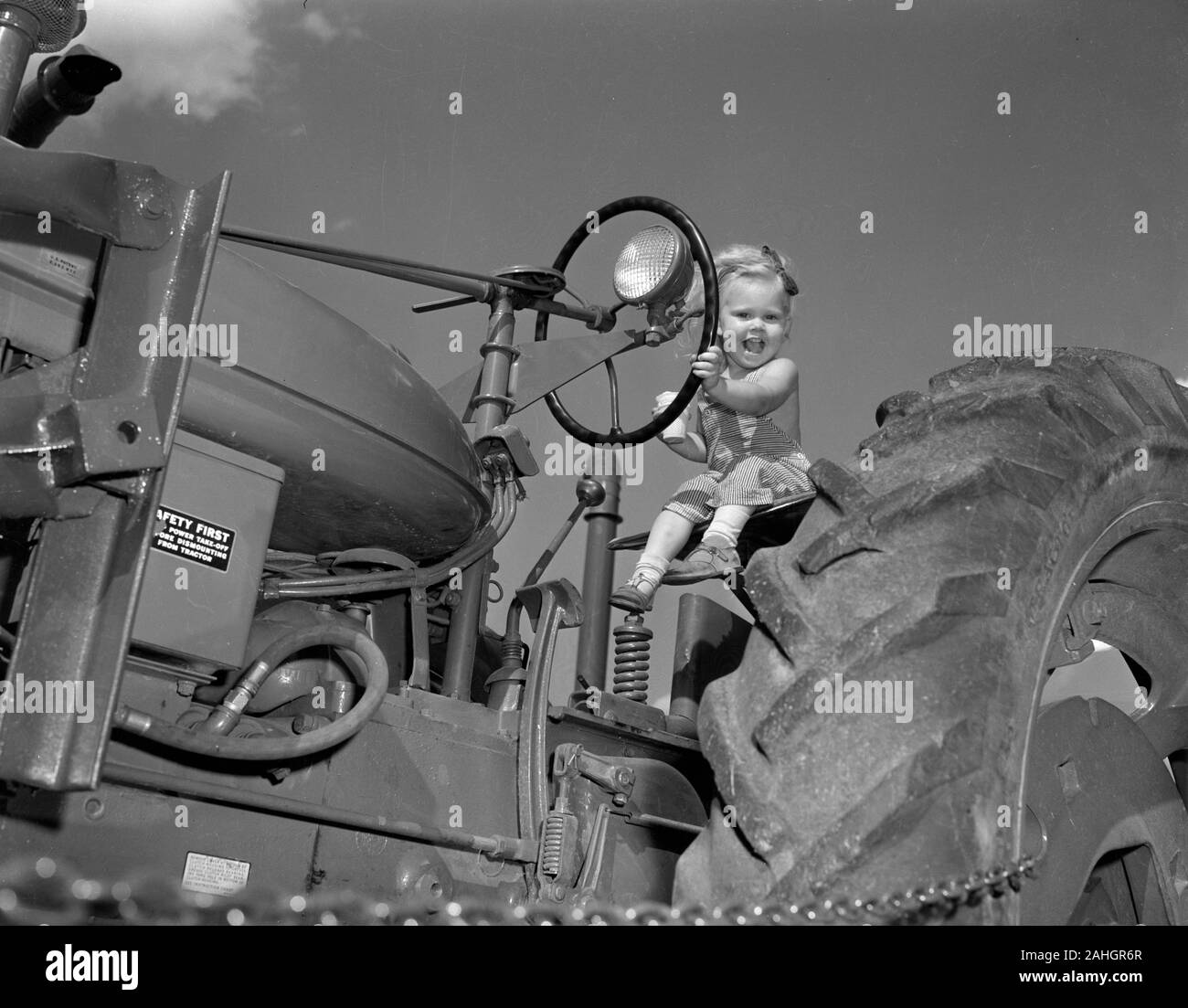 Une fille est assise sur un tracteur tout en mangeant de la crème glacée, 1946 Banque D'Images