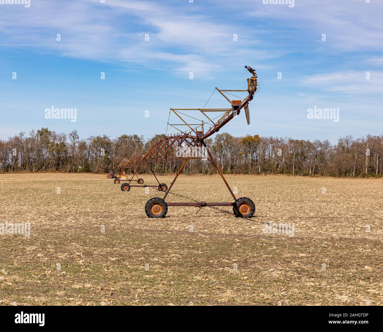 Rusty, ancien système d'irrigation à pivot central dans un champ avec des arbres récoltés, ciel bleu, et les nuages blancs en arrière-plan Banque D'Images