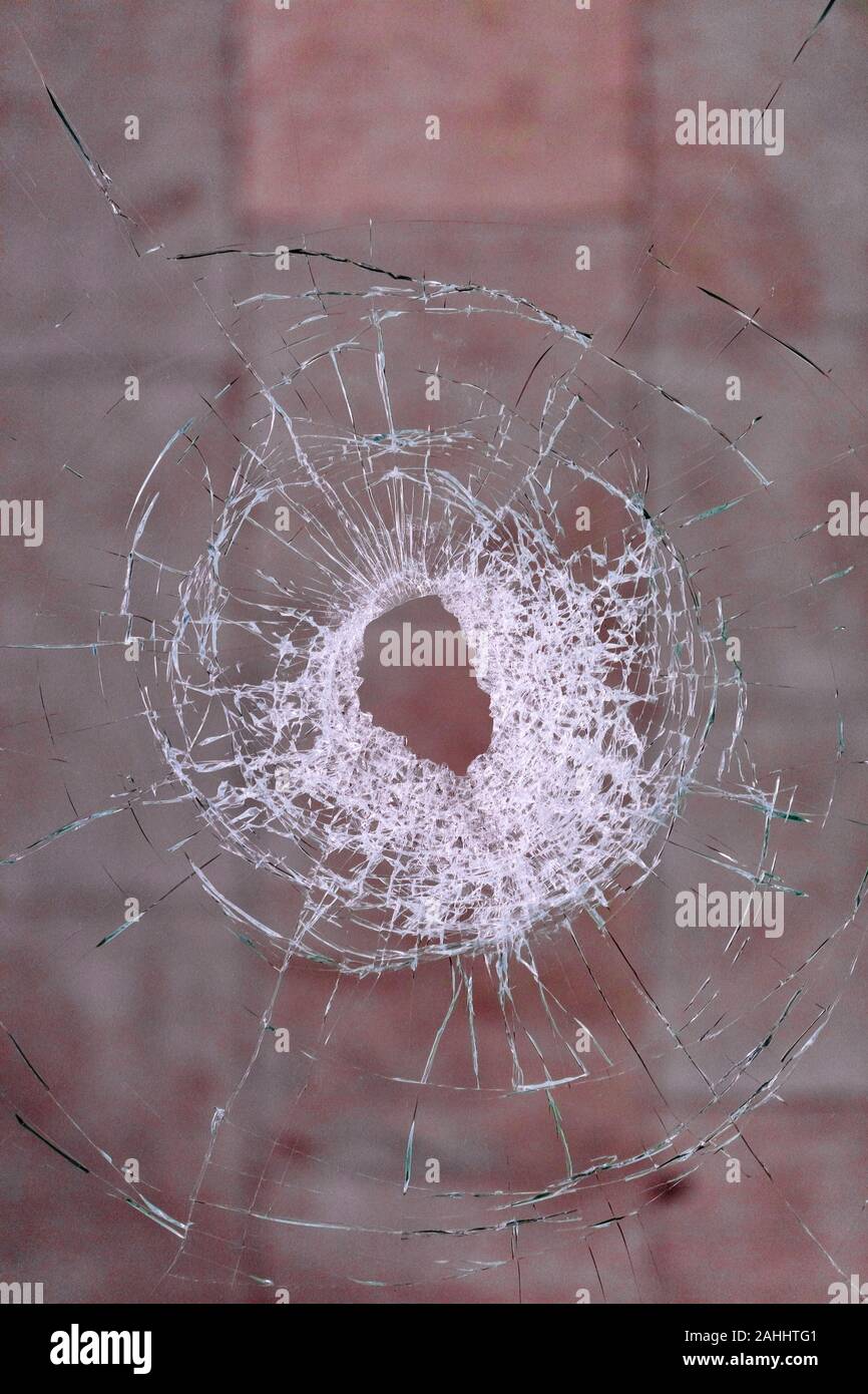Le trou de balle formes fissures radiales dans le verre contre un fond rouge sang, les images verticales avec copie espace. Banque D'Images