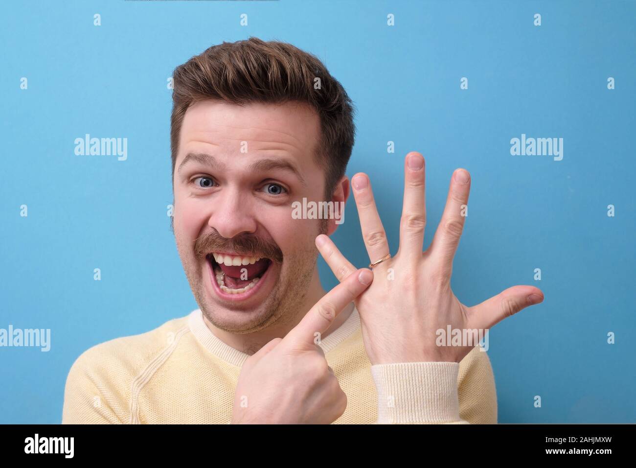 Heureux l'homme excité avec moustache pointant à l'anneau de mariage à son doigt Banque D'Images