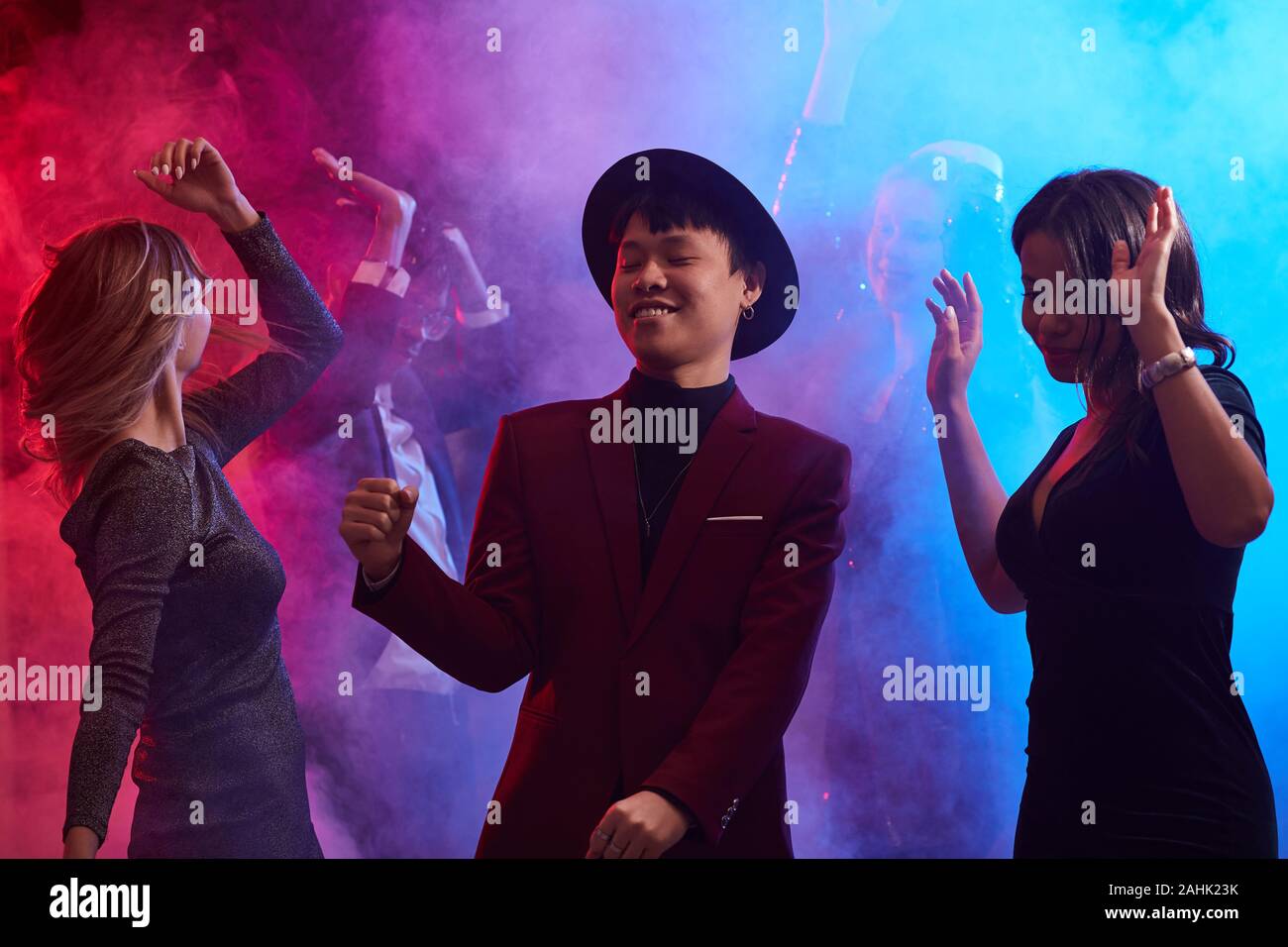 Jusqu'à la taille de la mode portrait Asian man dancing in smoky discothèque entouré de belles femmes, copy space Banque D'Images