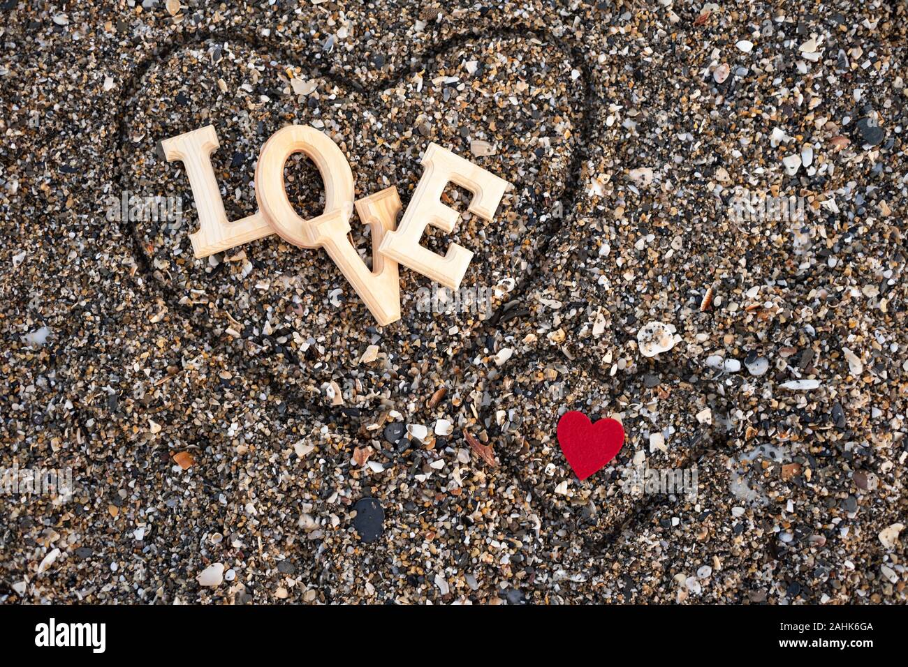 Lettres en bois formant le mot amour avec un cœur rouge sur un fond de sable de plage, à l'intérieur d'un coeur fait avec les doigts. concept de san valentin Banque D'Images