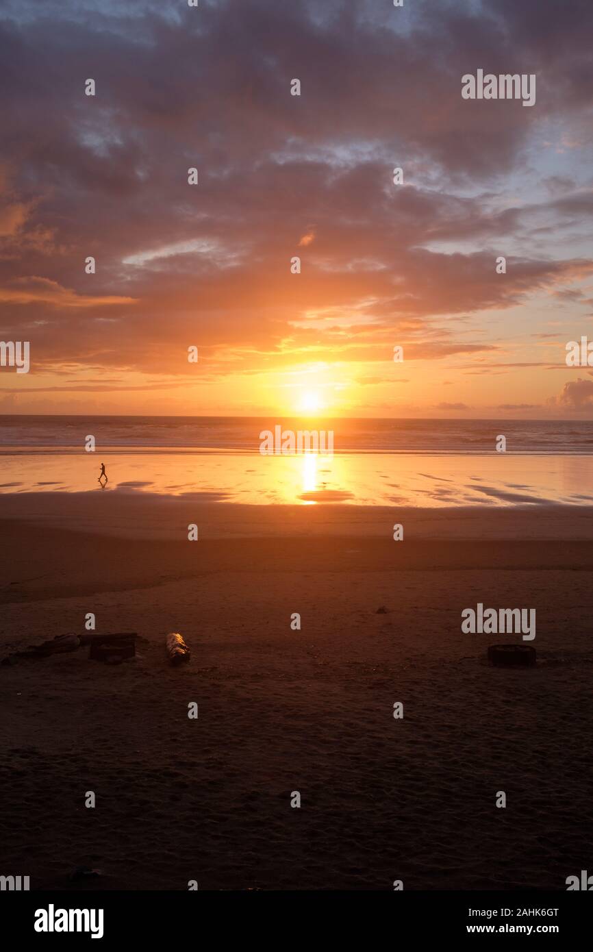 Petite silhouette de méconnaissable figure marchant sur la plage pendant un coucher de soleil d'or reposant sur Cannon Beach, ou. Banque D'Images