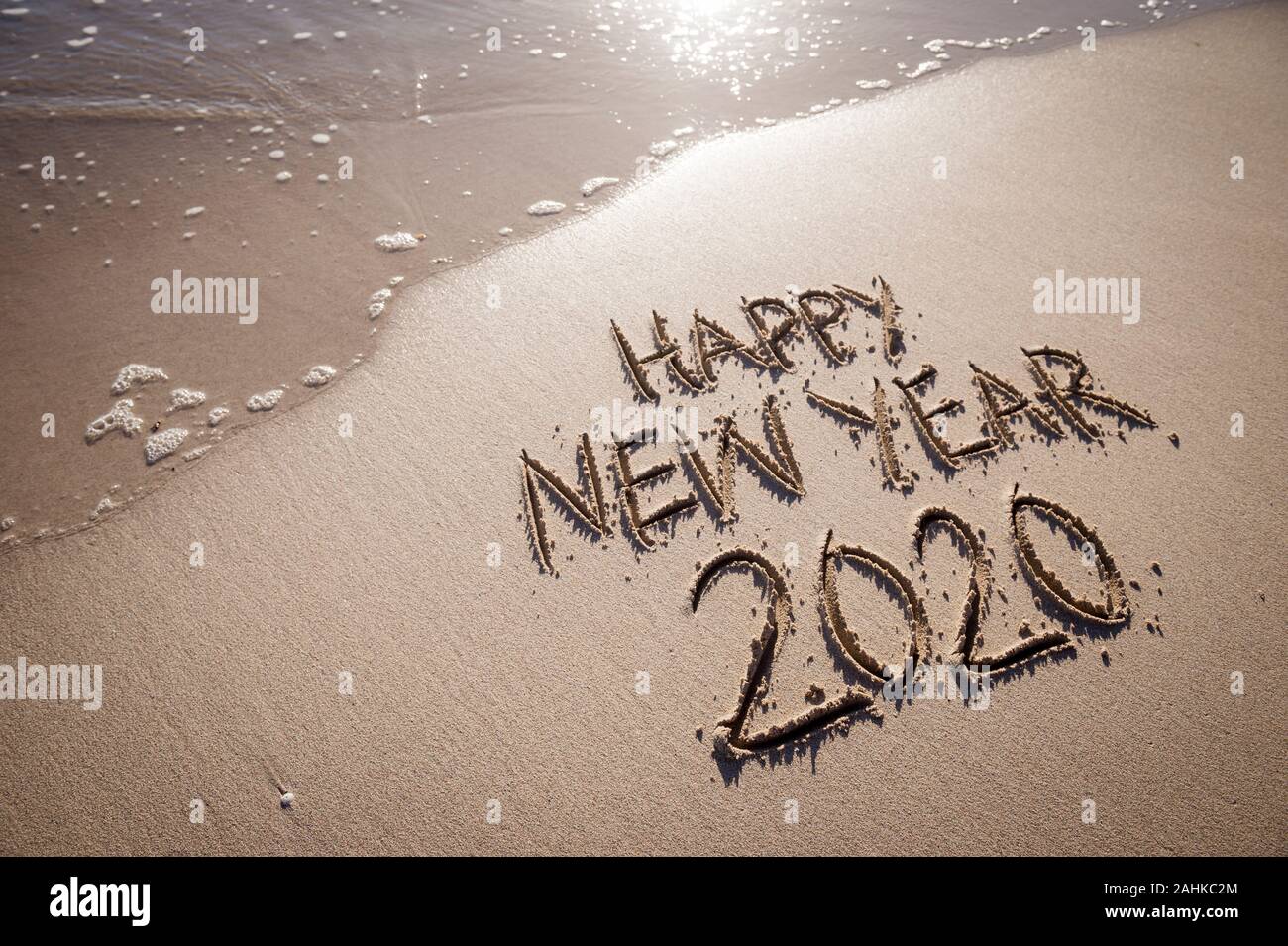 Bonne Année 2020 message écrits en lettres texturées relevée sur une plage de sable fin avec copie espace à côté d'onde Banque D'Images