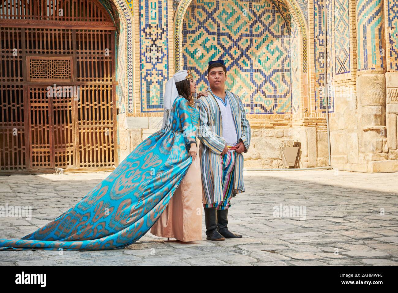 Couple de mariés en vêtements traditionnels posant devant de la célèbre place du Registan, Samarkand, Ouzbékistan, l'Asie centrale Banque D'Images