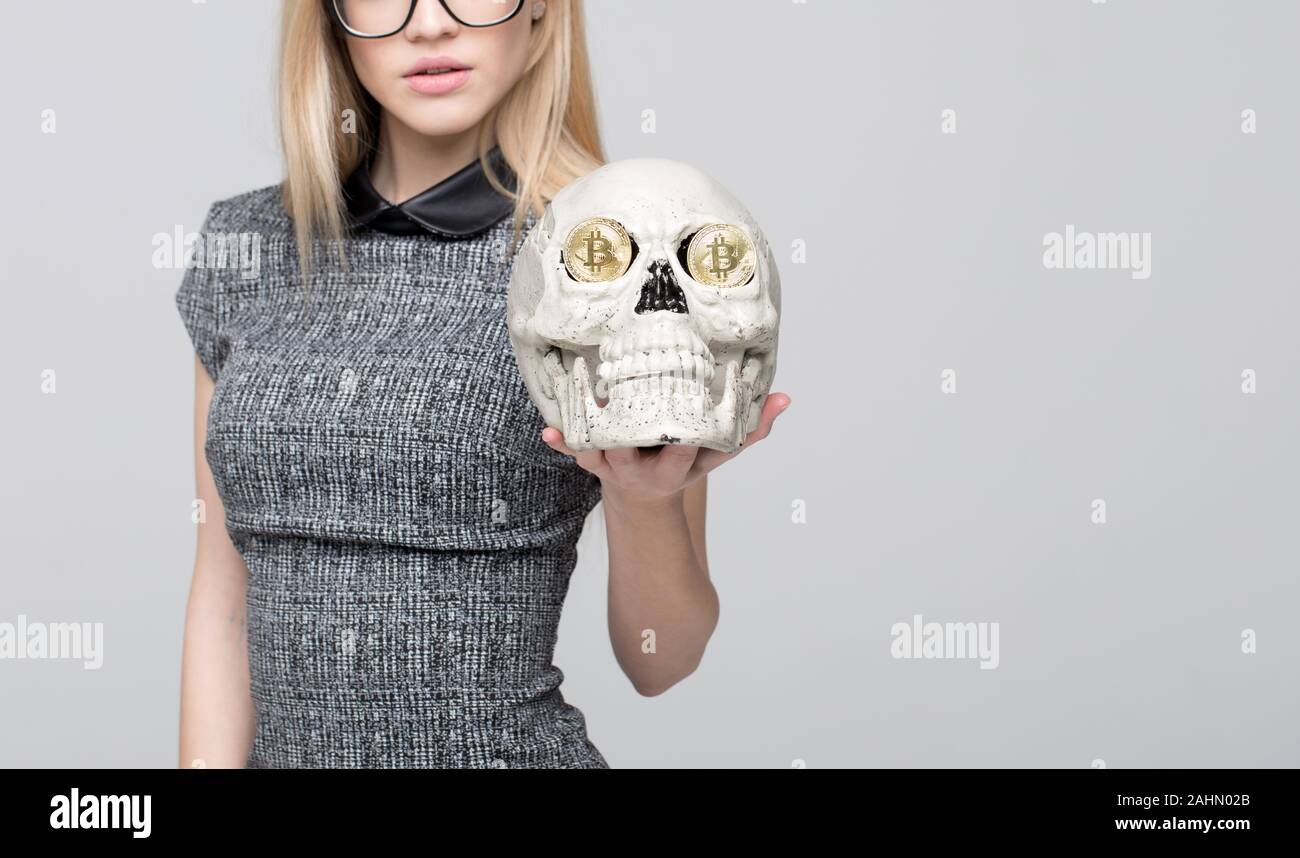 Femme blonde intelligente montrant le crâne avec des bitcoins en yeux concept sur fond gris Banque D'Images
