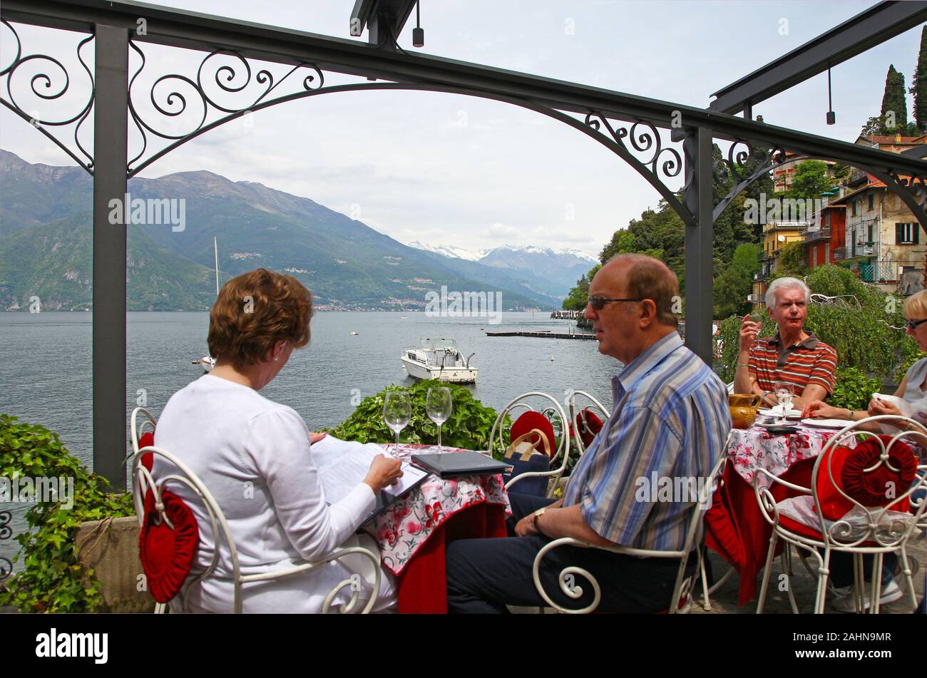 Les gens de manger à un restaurant en plein air ou dans un café donnant sur le lac de Côme Varenna Italie Banque D'Images