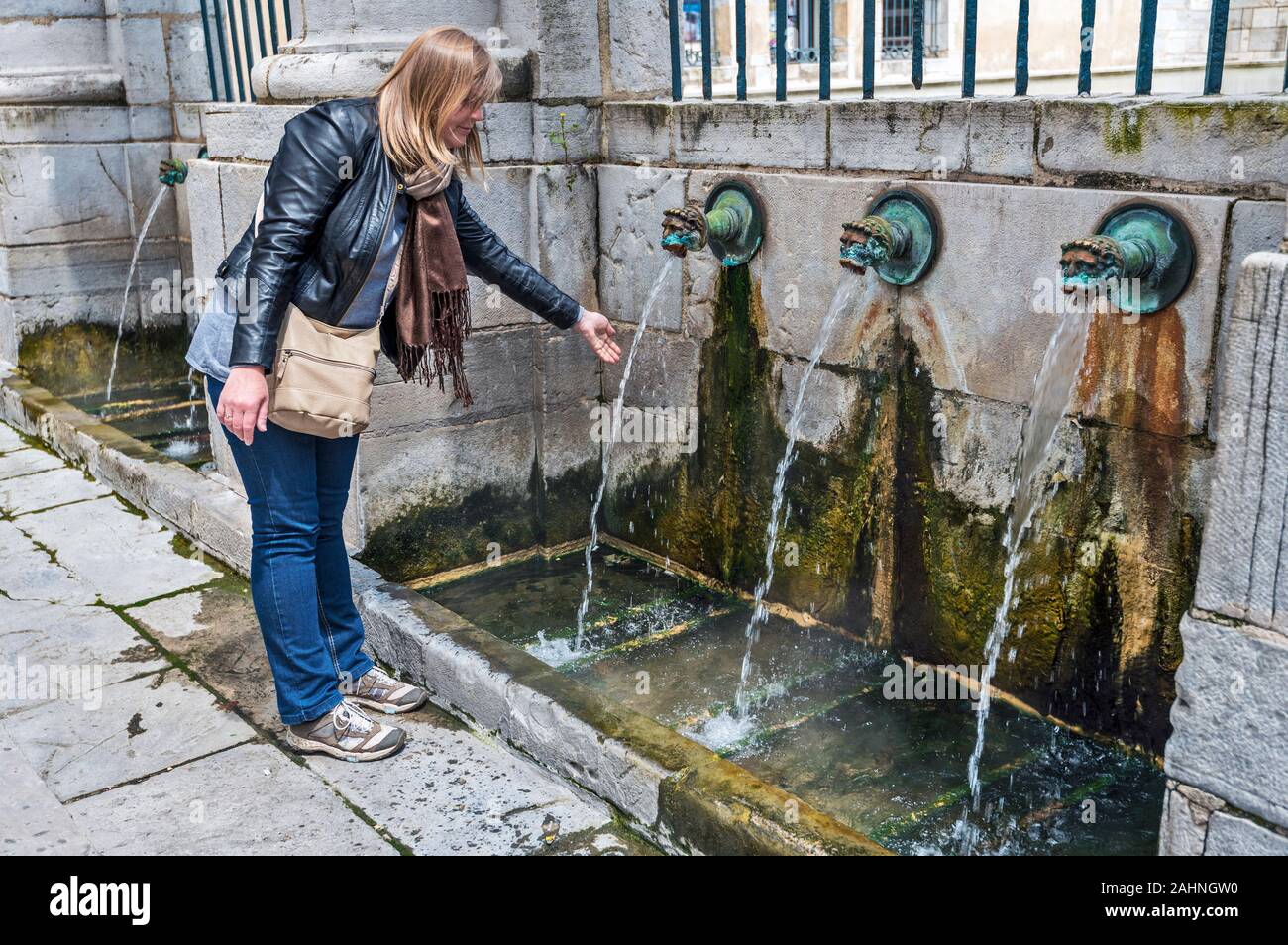 La femme est en contact avec le jet d'eau chaude de la source thermale dans le centre-ville de Dax. La région Aquitaine, Landes, Aquitaine Nouvelle. Banque D'Images