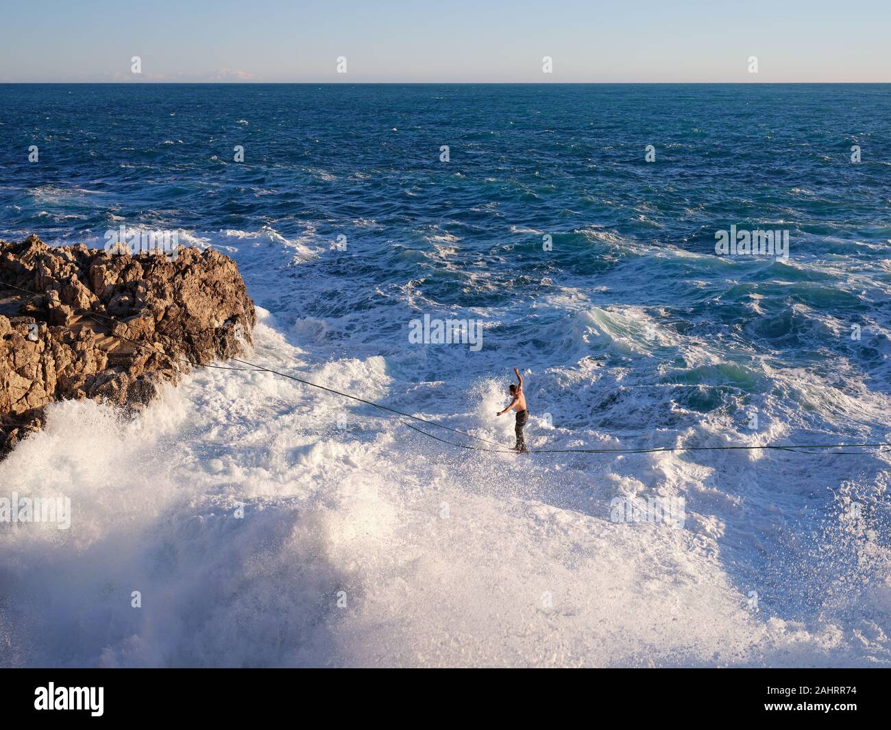 Le jeune homme se détend au-dessus de grandes vagues qui se brisent sur une côte rocheuse. Cap de Nice, Côte d'Azur, Alpes-Maritimes, France. Banque D'Images