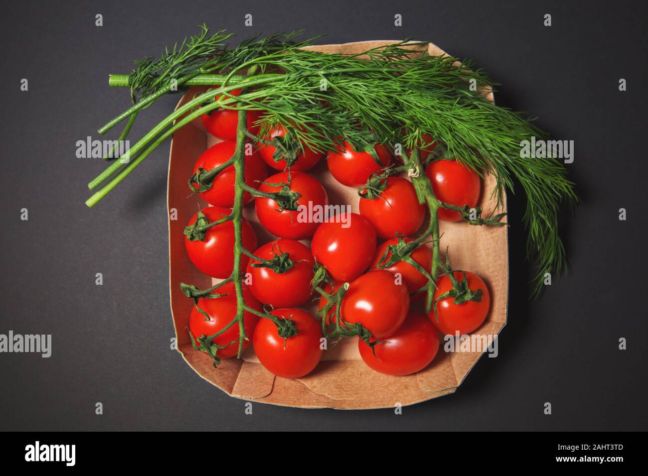 Tomates cerises rouges avec de l'aneth sur un fond noir dans une boîte en carton. Banque D'Images