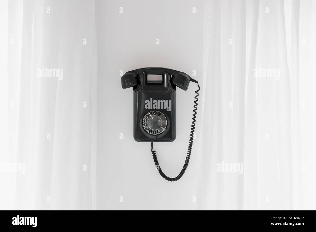 Vintage Téléphone à cadran noir accroché au mur, flanqué par des rideaux blancs Banque D'Images