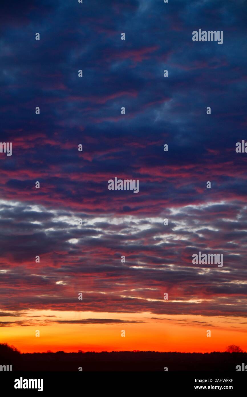 Beau lever de soleil : orange, rouge et bleu foncé nuages sur un horizon noir Banque D'Images