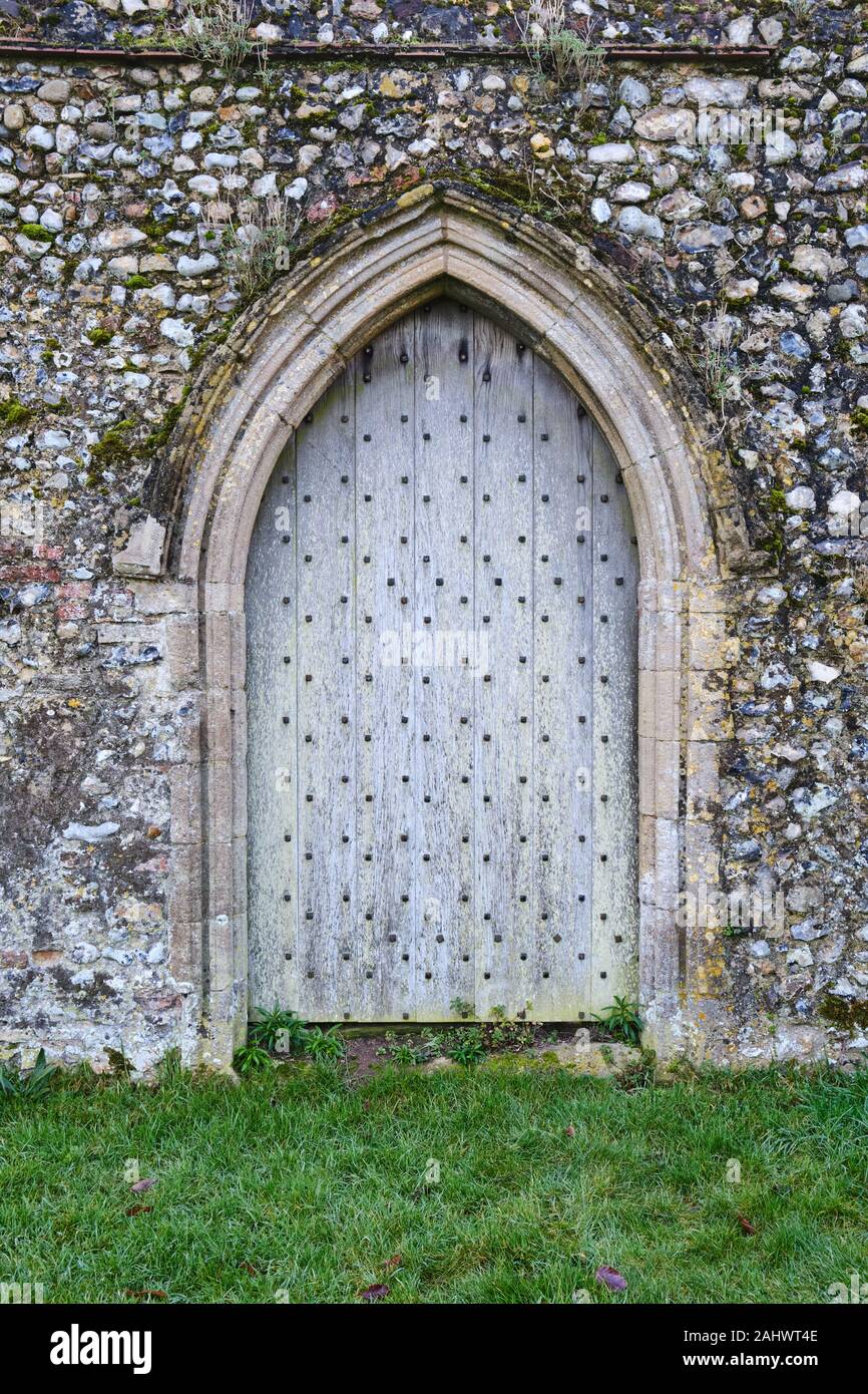 Un passage voûté en forme pâle porte antique en bois noir avec clous dans une arche en pierre avec l'herbe en premier plan vieux mur de pierre Banque D'Images