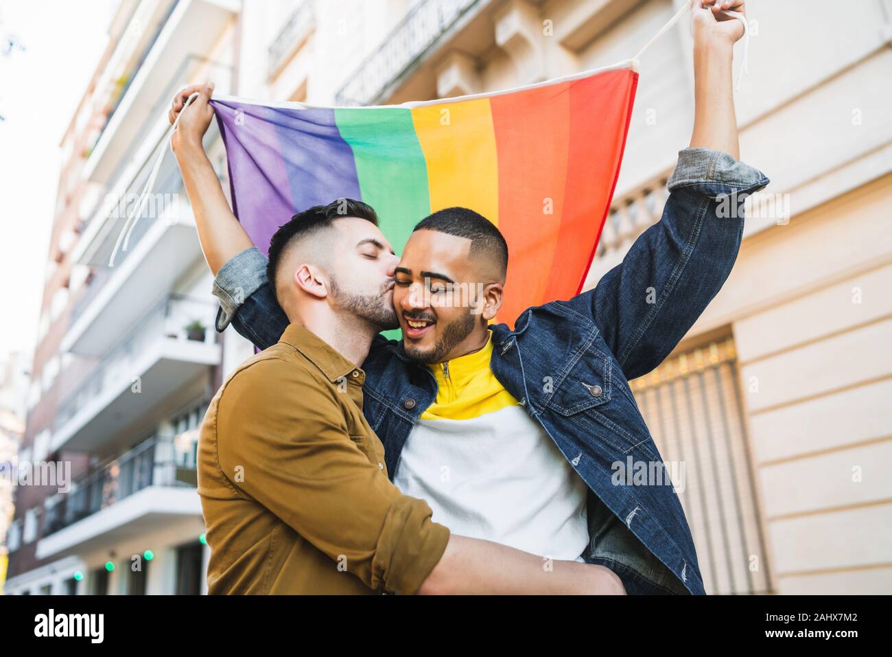 Portrait of young couple embracing et montrant leur amour avec drapeau arc-en-ciel à la rue. Amour LGBT et concept. Banque D'Images
