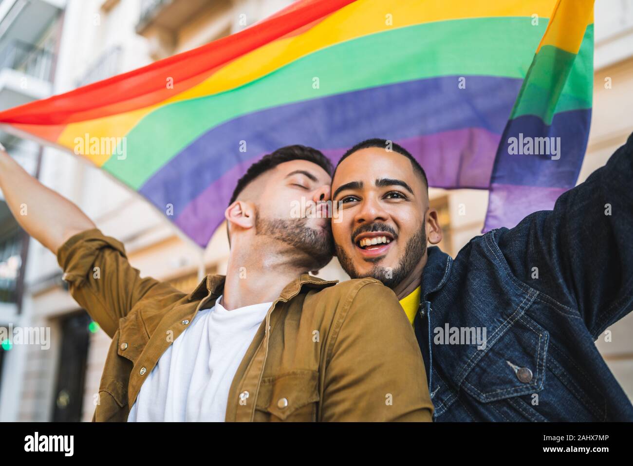 Portrait of young couple embracing et montrant leur amour avec drapeau arc-en-ciel à la rue. Amour LGBT et concept. Banque D'Images