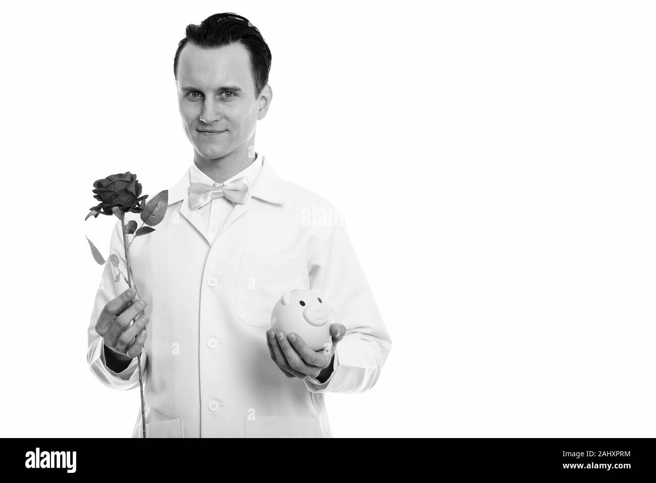 Portrait de jeune homme doctor holding red rose and piggy bank Banque D'Images