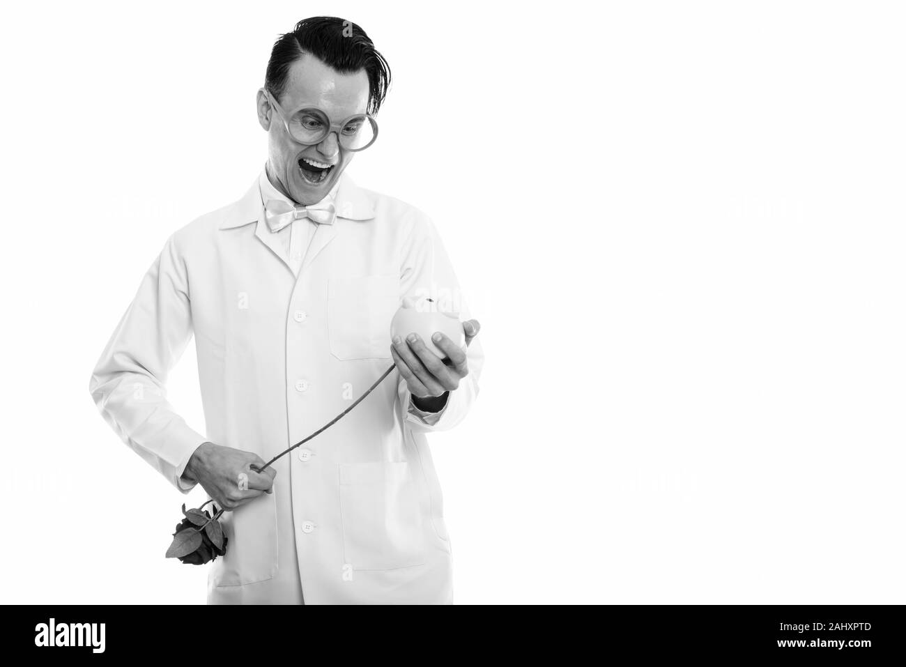 Studio shot of happy crazy man smiling médecin tout en poignardant rose rouge à l'intérieur de Piggy Bank Banque D'Images