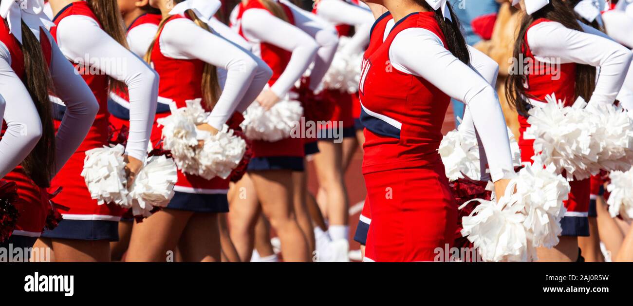 High school cheerleaders porter du rouge, blanc et bleu applaudissent pendant un match de football holding pompons blancs. Banque D'Images