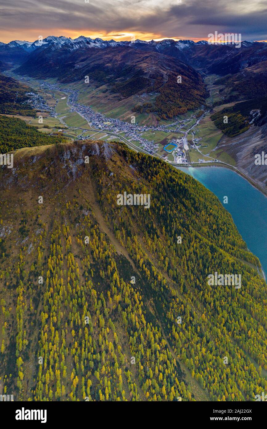 Coucher de soleil sur forêts de mélèzes sur crap de la tape crête en direction du village de Livigno et le lac, vue aérienne, la Valtellina, Lombardie, Italie, Europe Banque D'Images