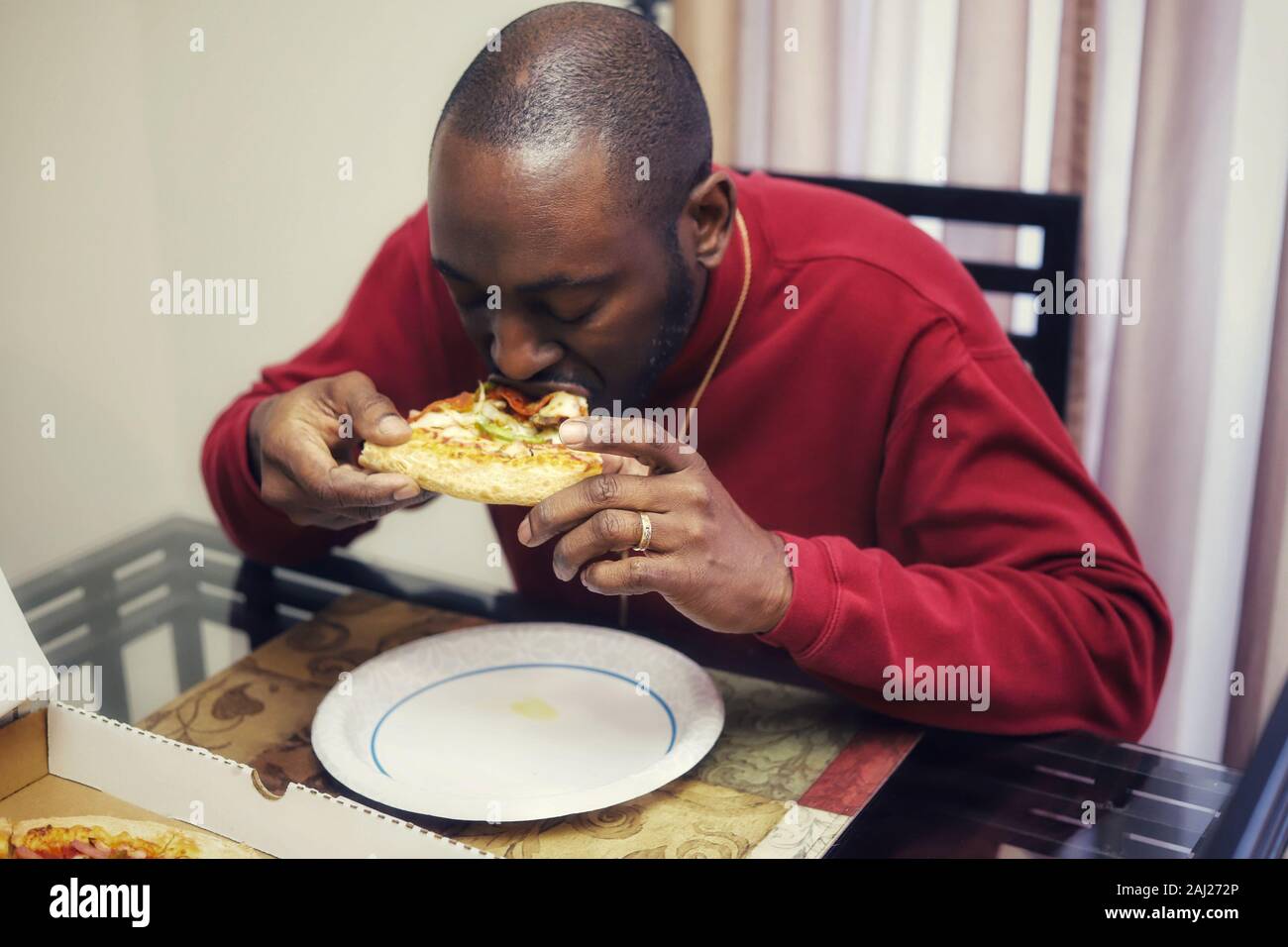 L'homme afro-américain de manger une tranche de pizza à la maison Banque D'Images