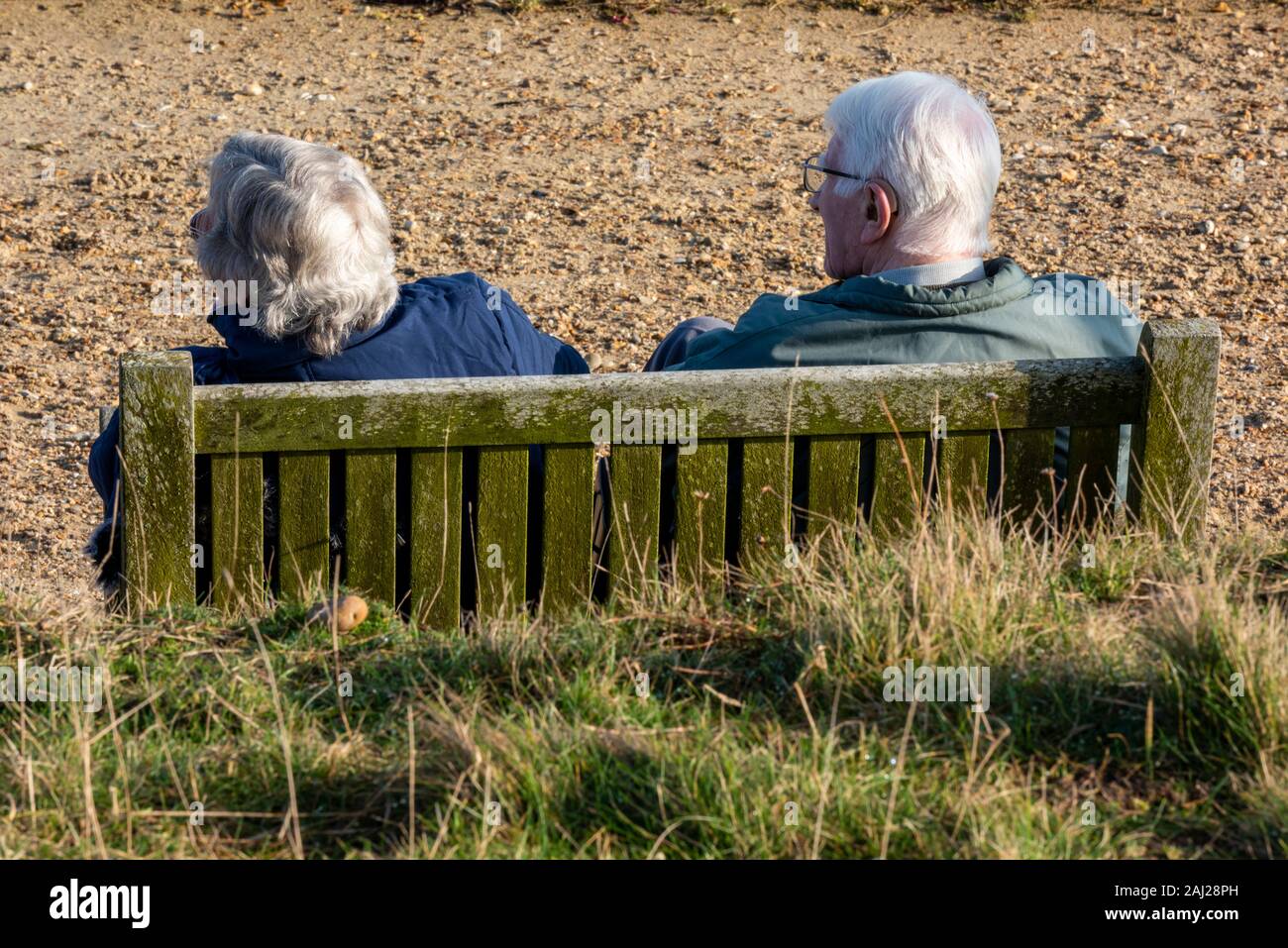 Un vieux couple de retraités aux cheveux gris homme et femme assis sur un banc au bord de il regardant la mer ensemble, Banque D'Images