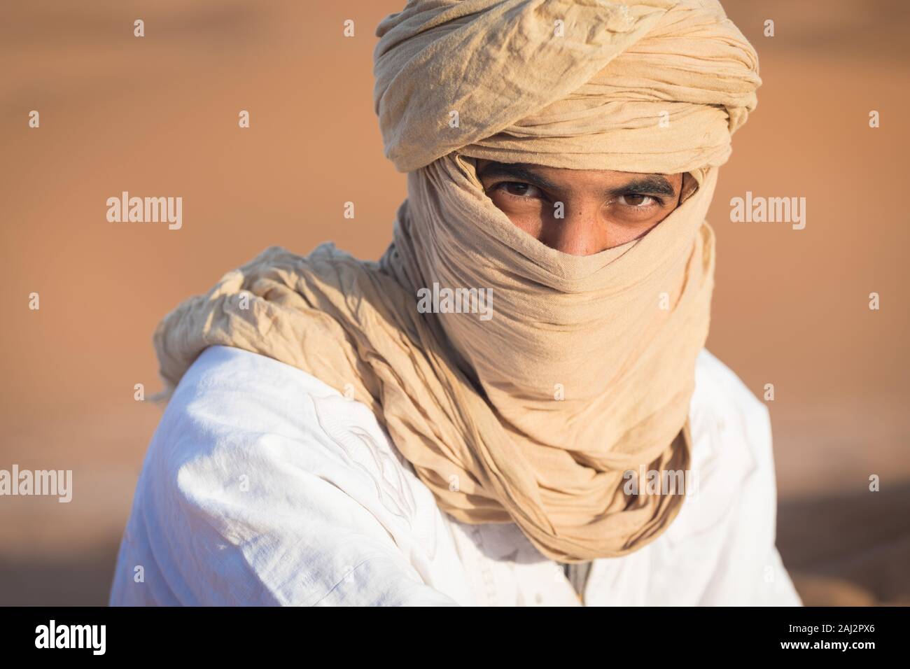 Portrait d'un Bédouin nomad avec turban coloré et grand sourire assis sur dune de sable touristique populaire Merzouga désert. Homme Touareg Banque D'Images