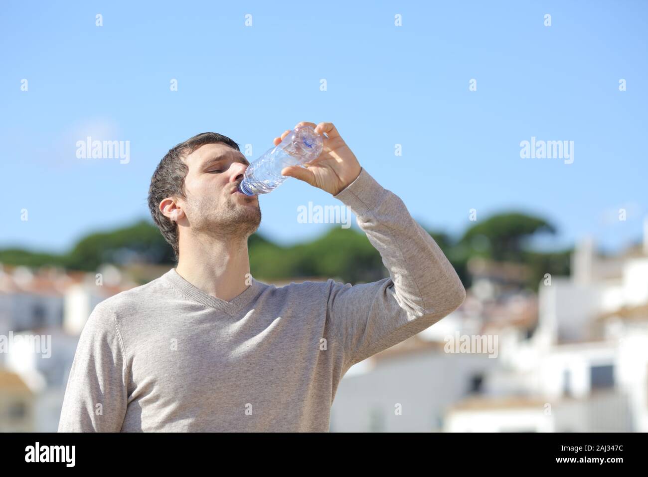 Casual homme adulte de boire de l'eau en bouteille debout dans une ville rurale d'une journée ensoleillée Banque D'Images