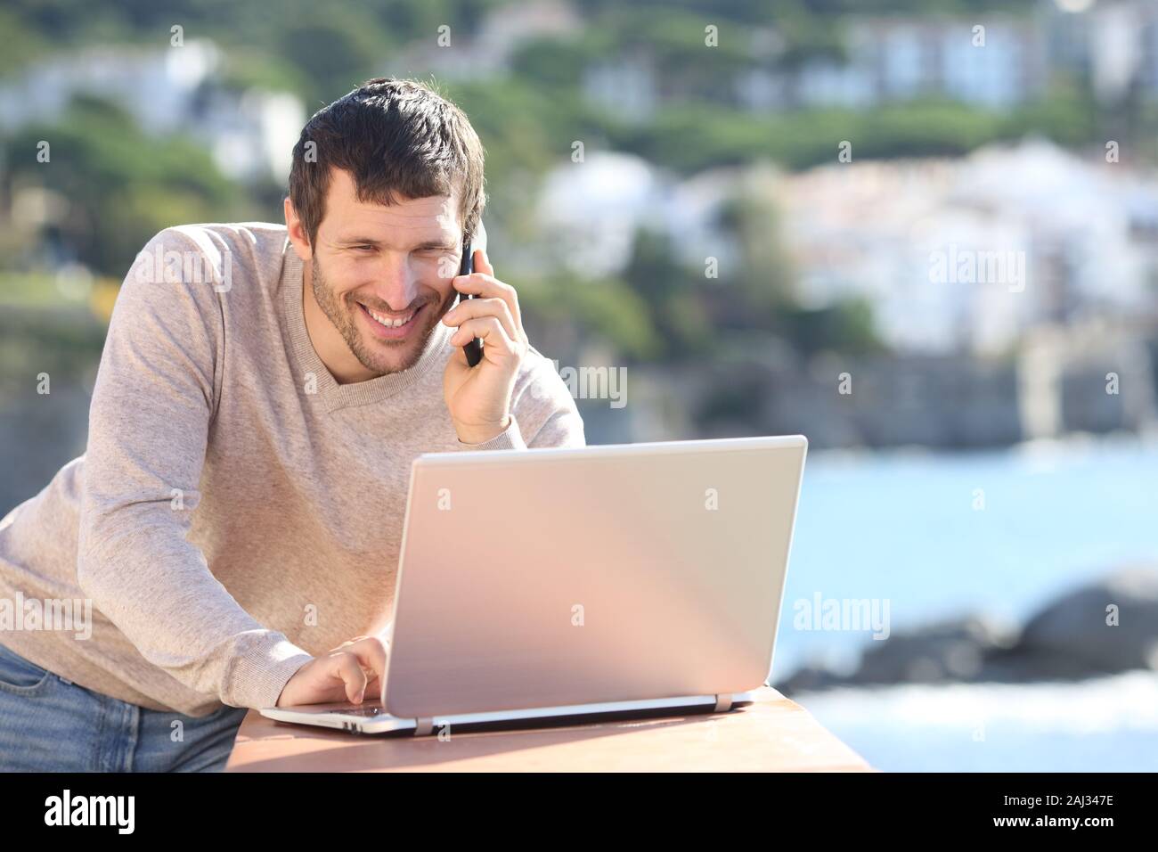Heureux hot man using laptop and talking on smart phone dans un balcon sur la plage Banque D'Images