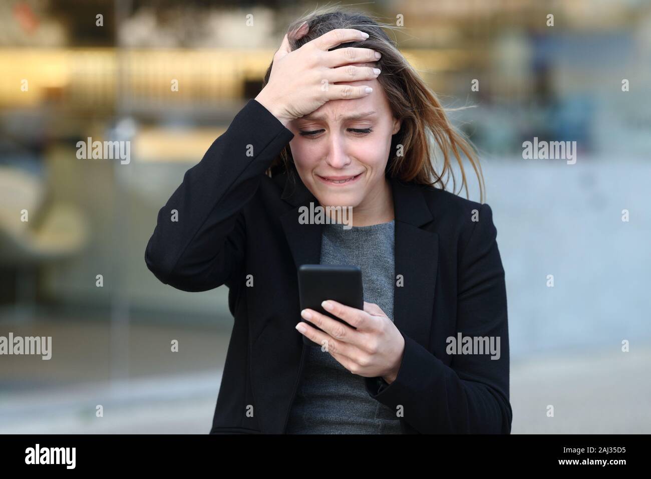 Vue de face d'une triste plainte exécutif contrôle smart phone dans la rue à côté d'office Banque D'Images