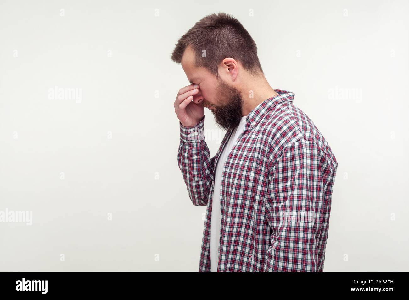 Vue de côté portrait de malheureux homme barbu en chemise à carreaux décontractée debout avec la tête en bas, se frotter les yeux et de pleurer, fatigué d'humeur dépressive. lieu vide fo Banque D'Images