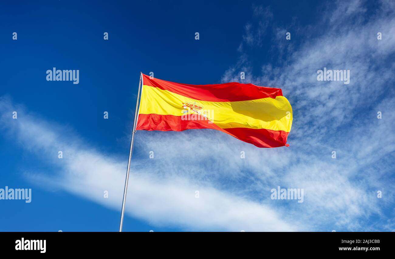Drapeau espagnol sur un poteau, ondulant dans le vent sur ciel bleu avec des nuages blancs Banque D'Images