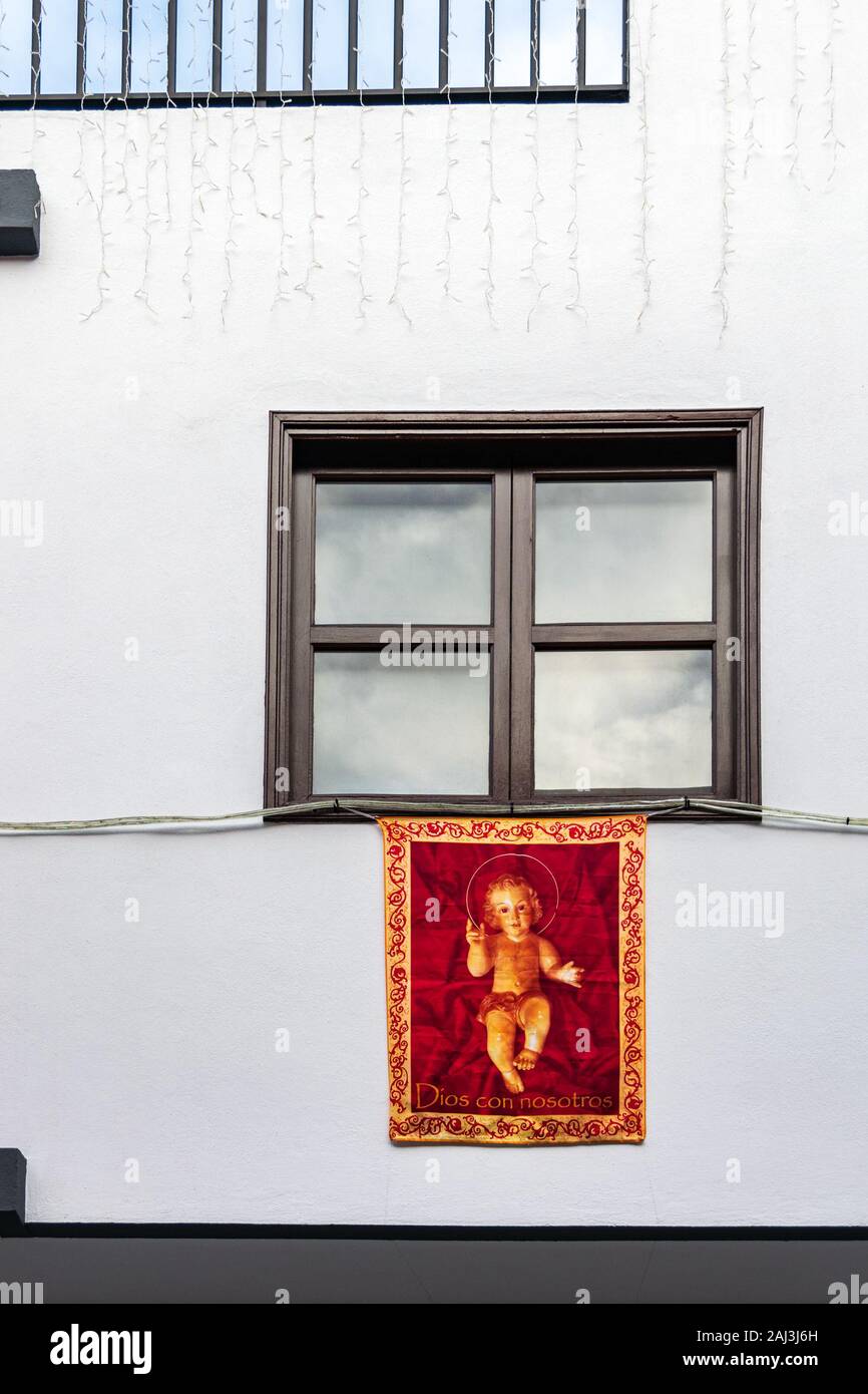 Drapeau rouge représentant l'Enfant Jésus suspendu à la fenêtre d'un bâtiment blanc en Garachico, Tenerife, Espagne. C'est une tradition de Noël espagnol. Banque D'Images