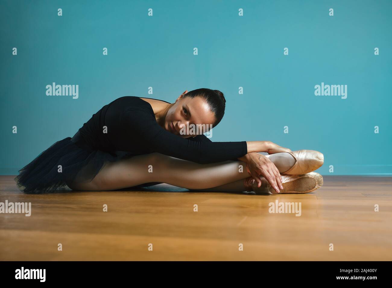 Jolie femme ballerine en tutu et pointe en noir Maillot de posing in studio sur fond bleu. Banque D'Images
