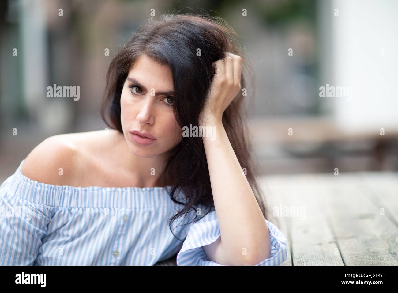 Une belle jeune femme assise à la table dans un parc de la ville, regardant au loin Banque D'Images