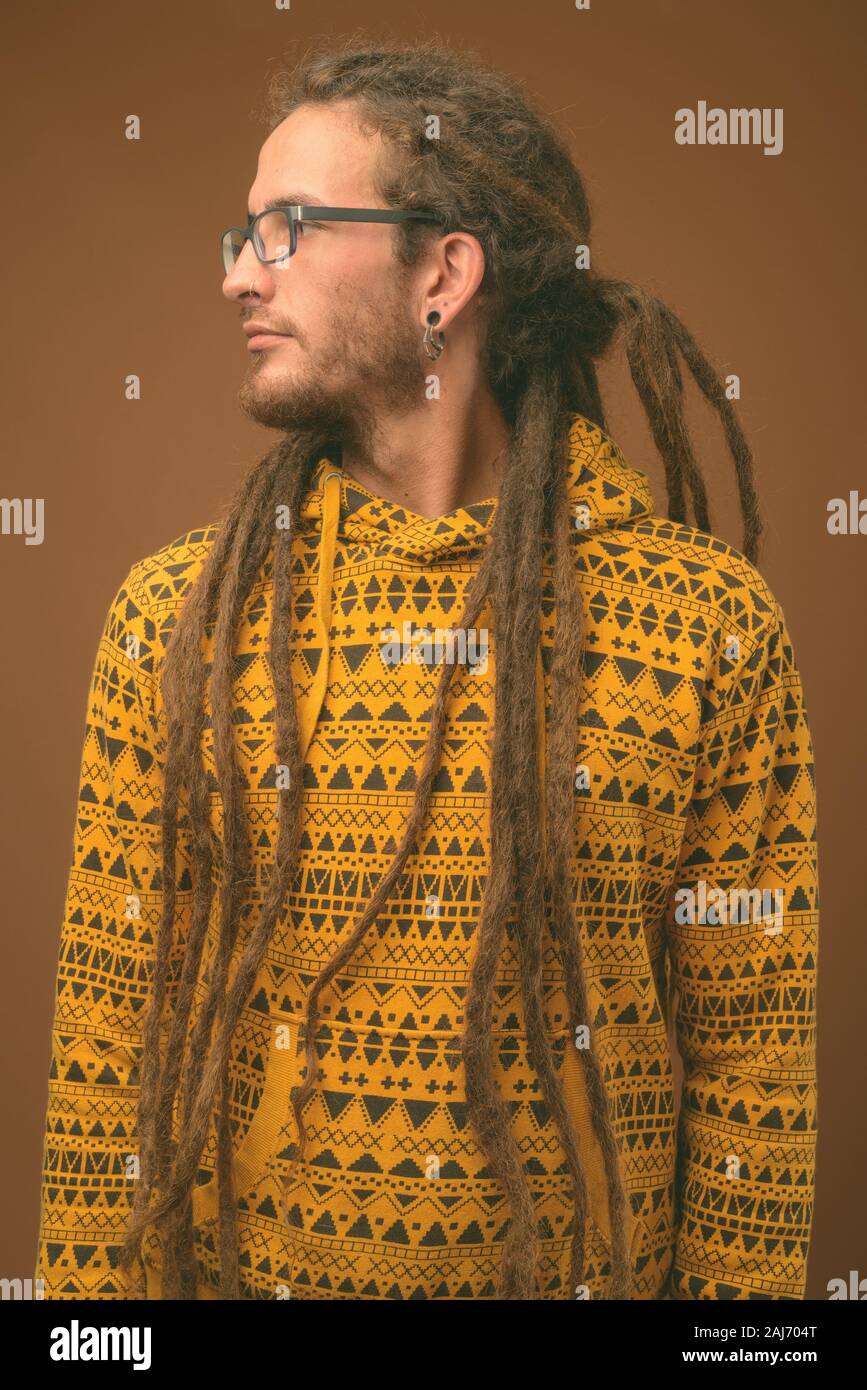 Studio shot of young handsome man avec des dreadlocks wearing hoodie contre fond brun Banque D'Images