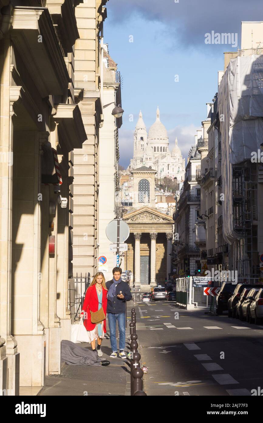Rue de Paris - un couple en train de marcher le long de la rue ensoleillée à Paris avec la basilique du Sacré-Cœur à l'arrière-plan. La France, l'Europe. Banque D'Images