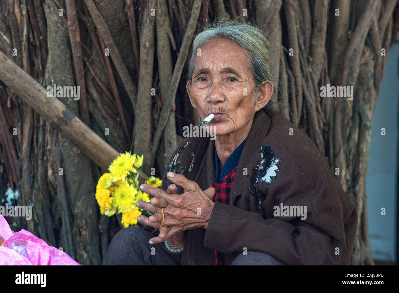 Une vieille femme asiatique fumer une cigarette mains jointes Banque D'Images