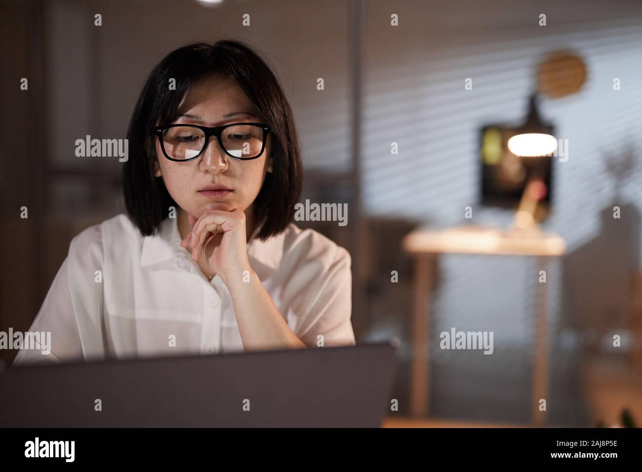 Asian pensive businesswoman wearing eyeglasses à surveiller à son ordinateur portable et de travailler au bureau Banque D'Images