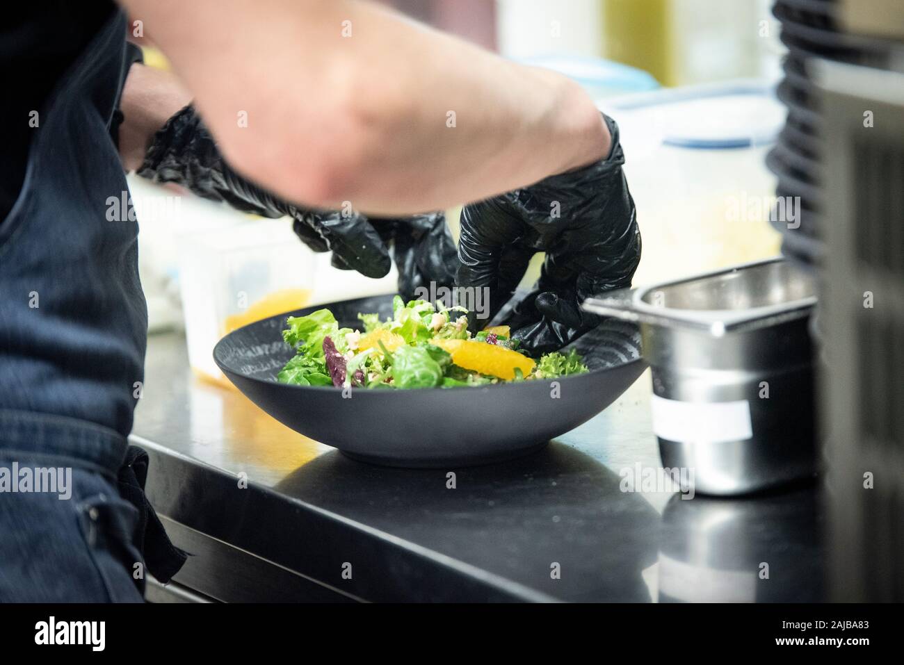 Gros plan sur les mains d'un cuisinier préparer une salade dans une cuisine avec des gants en plastique noir Banque D'Images