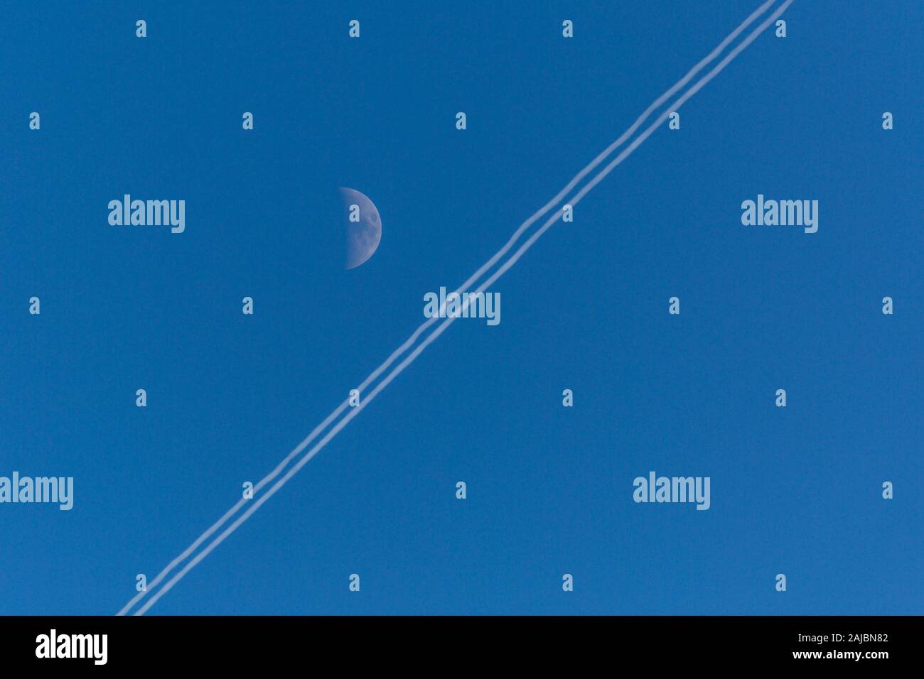 Ciel bleu avec blanc de la demi-lune et de traînée de condensation sur une journée d'hiver ensoleillée. Banque D'Images